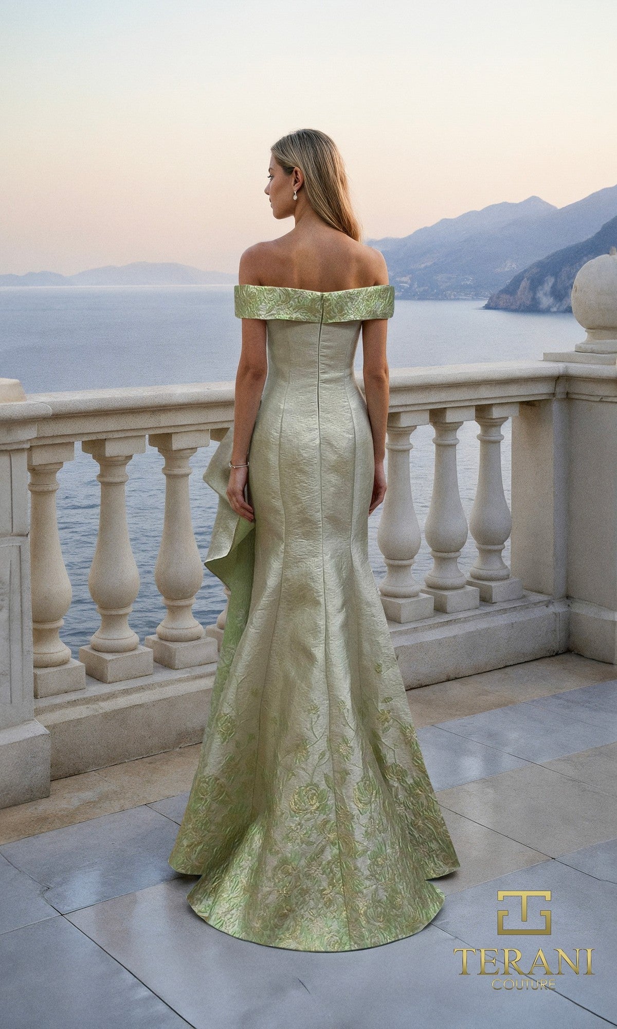 A woman in an off-the-shoulder, light green jacquard Long Formal Dress (Terani 261M6451) stands on a stone terrace overlooking the sea and distant mountains. The Terani Couture logo appears in the bottom right corner.